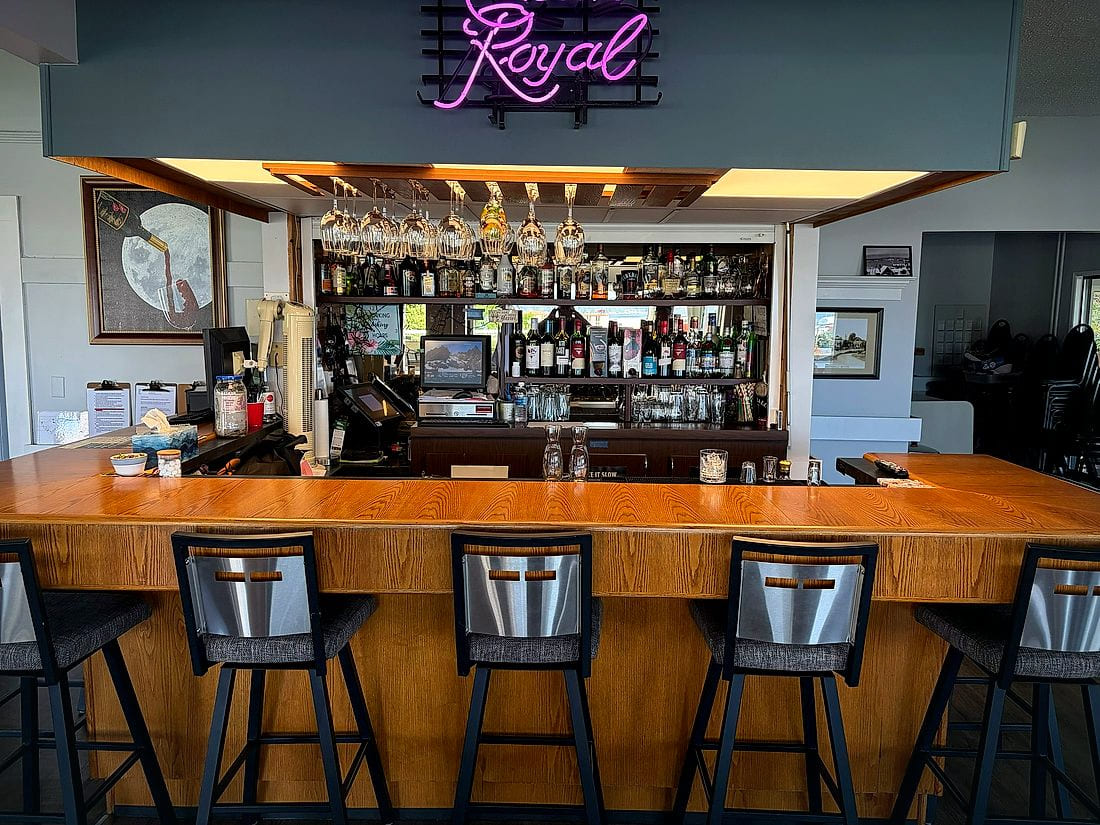 The Club's bar with hanging glasses, well-stocked shelves and a neon sign