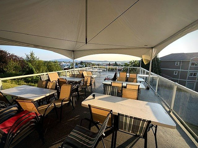 The Club's deck set with tables under the marquee, overlooking downtown and the Strait at golden hour